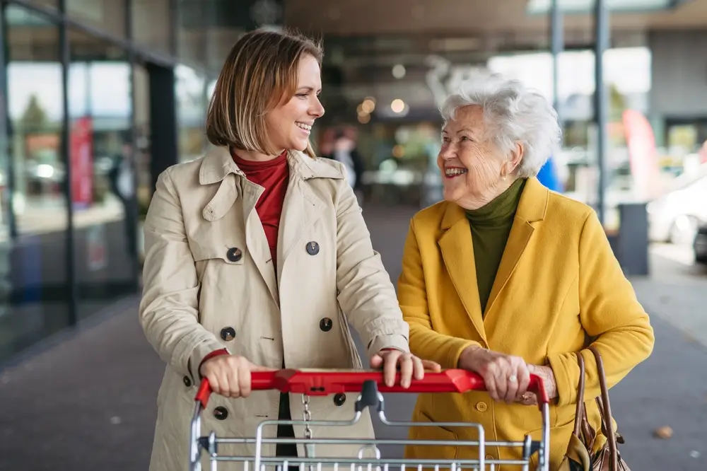 Mature granddaughter taking her grandmother shopping at the shopping center. Senior woman needs help with grocery shopping.