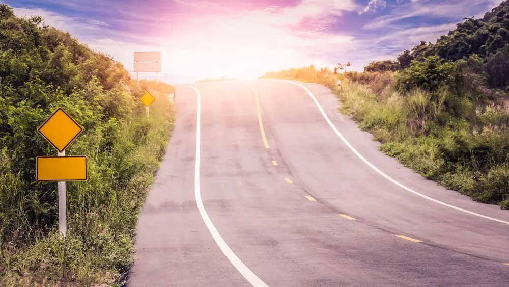 Asphalt concrete road across tropical forest along up to hill with traffic sign and sunlight shining, Concept of journey