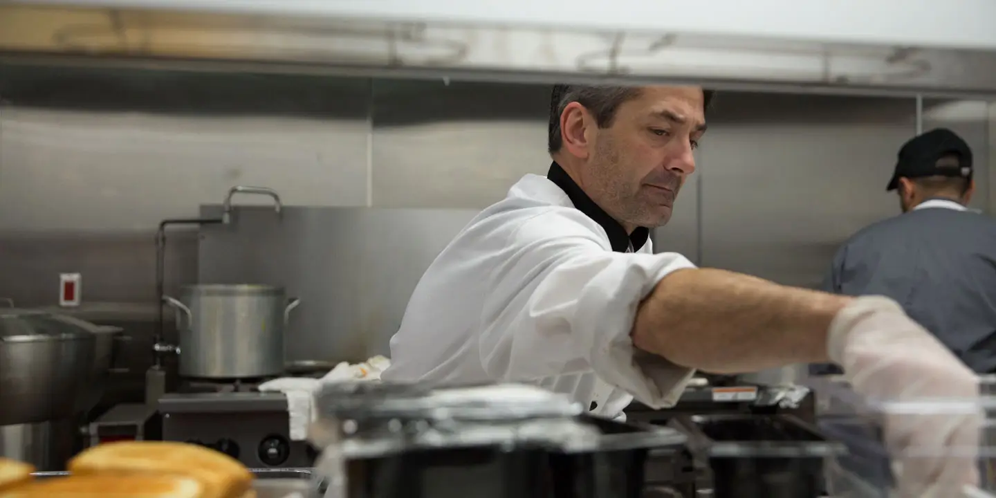 A head chef reaching into a container to get an ingredient to spice up the main dish.