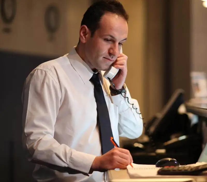 Concierge on the phone with a customer, writing in his work planner.