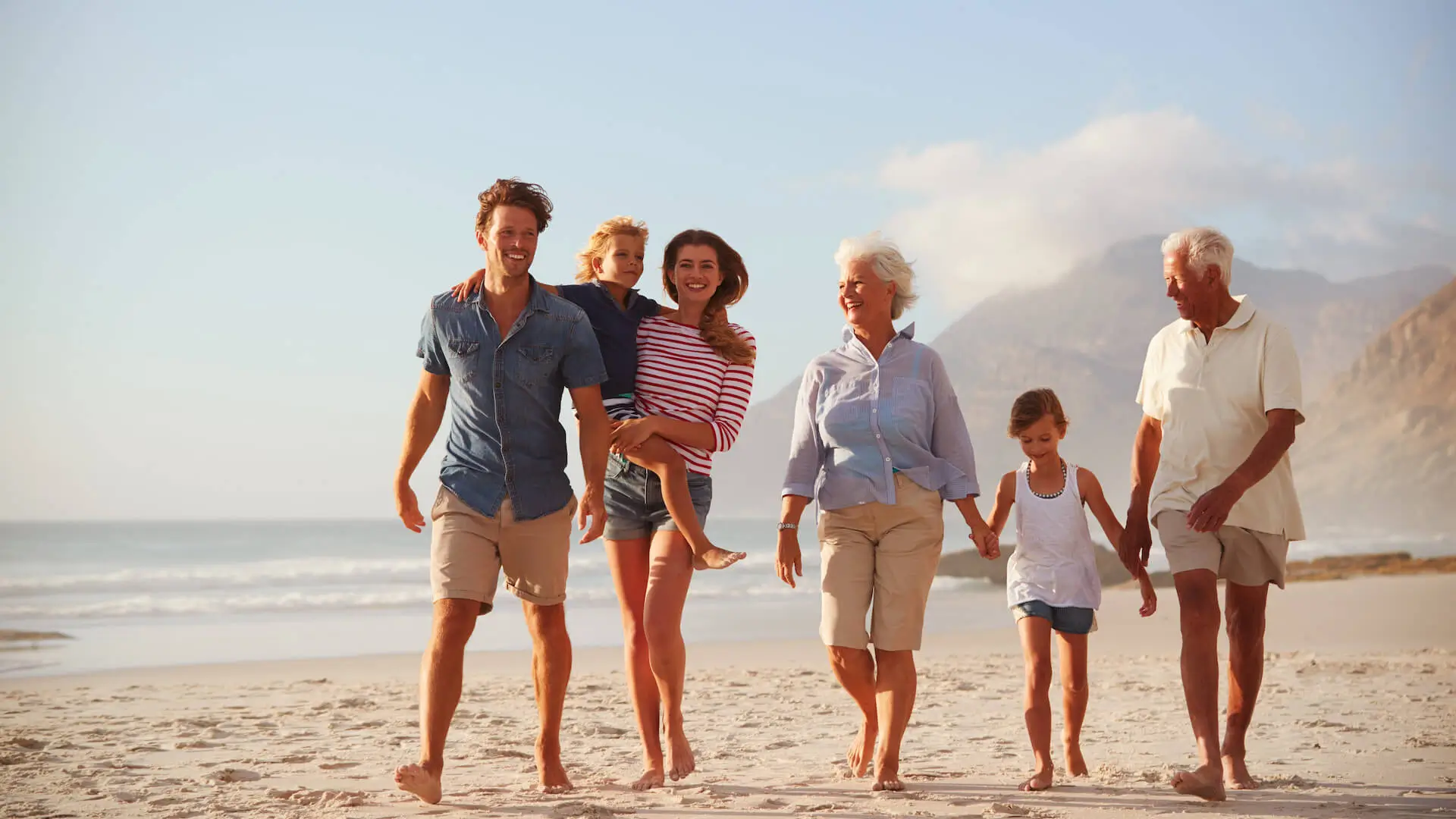 Multi Generation Family On Vacation Walking Along Beach Together