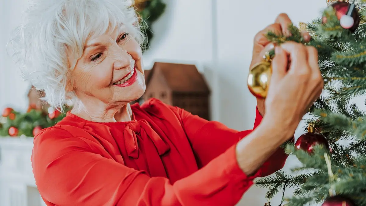 Senior decorating her Christmas Tree with a gold ornament