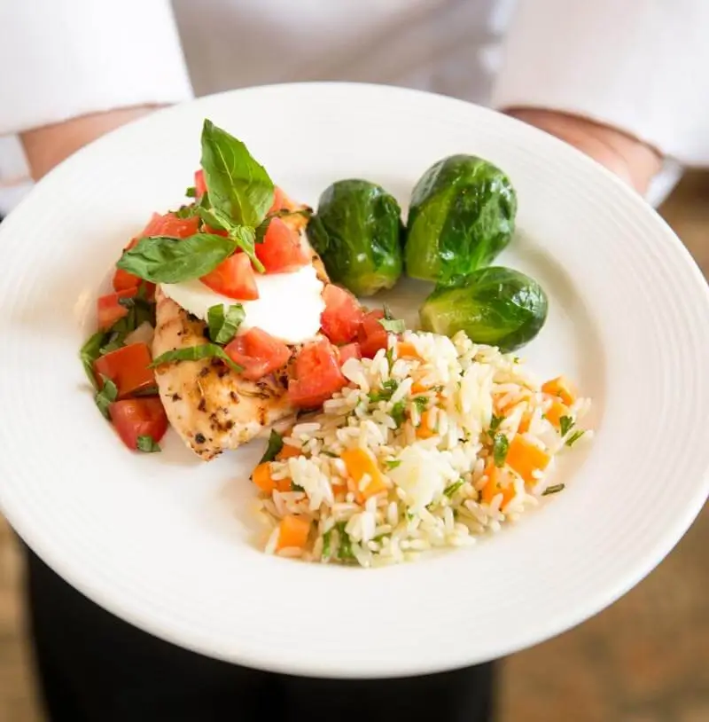 Culinary teammate showing off a colorful dish of chicken, rice, and brussels sprouts.