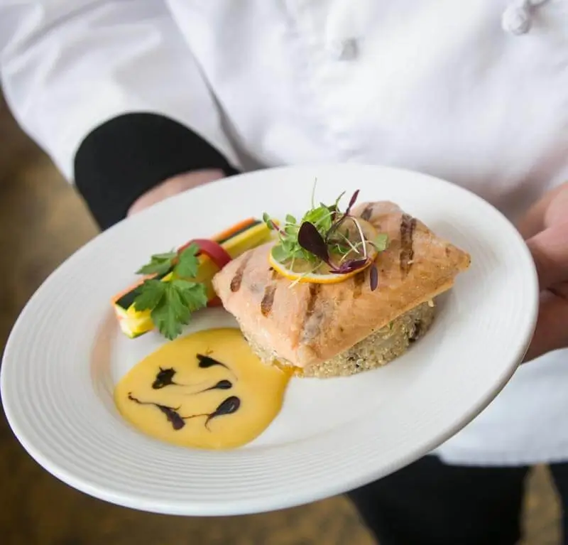 Culinary teammate showing off a colorful dish of salmon, zucchini, and quinoa.