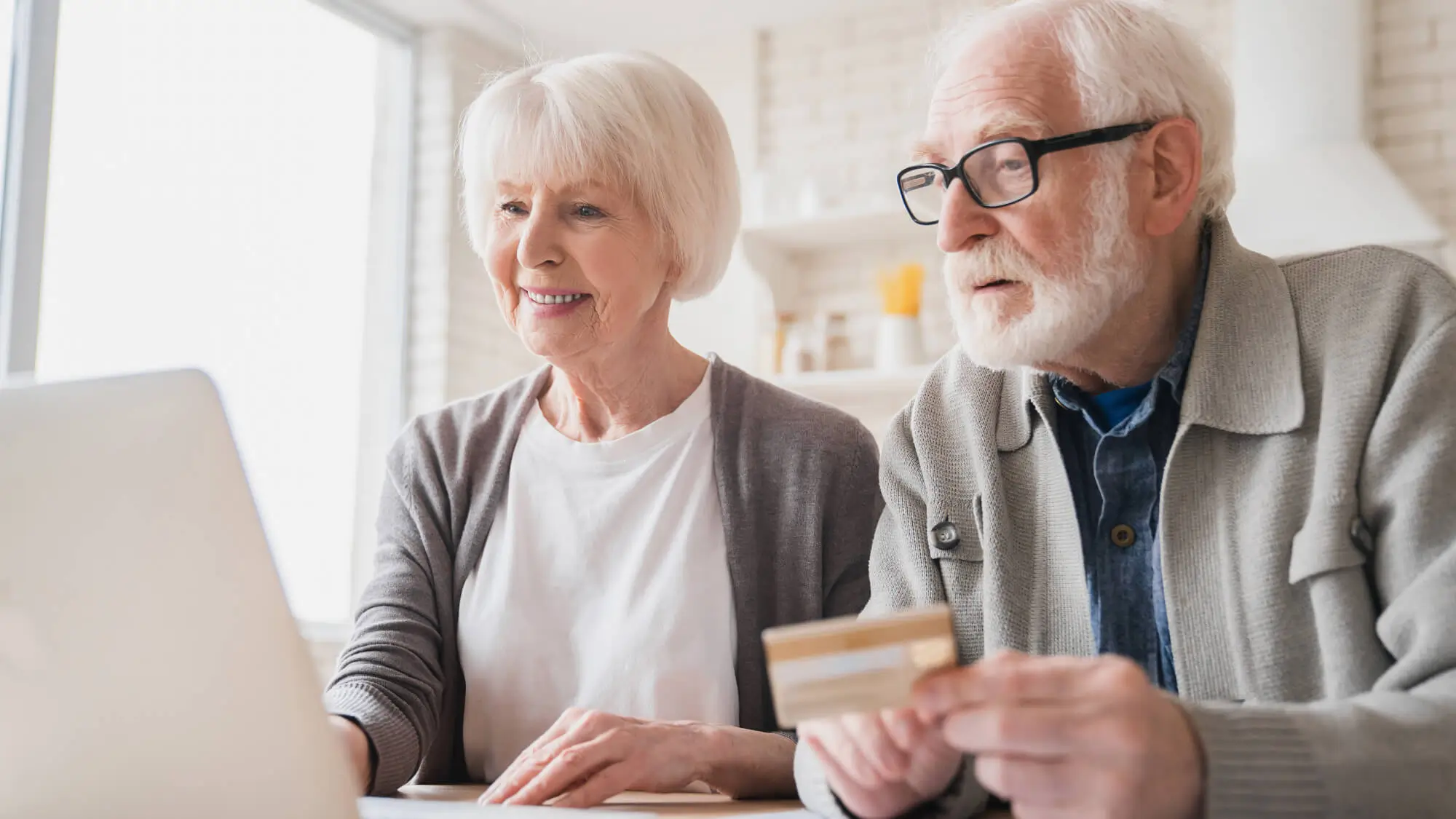 Smart old senior elderly caucasian couple grandparents husband and wife receiving pension paying domestic bills, doing online shopping with credit card and laptop, e-banking and e-commerce at home