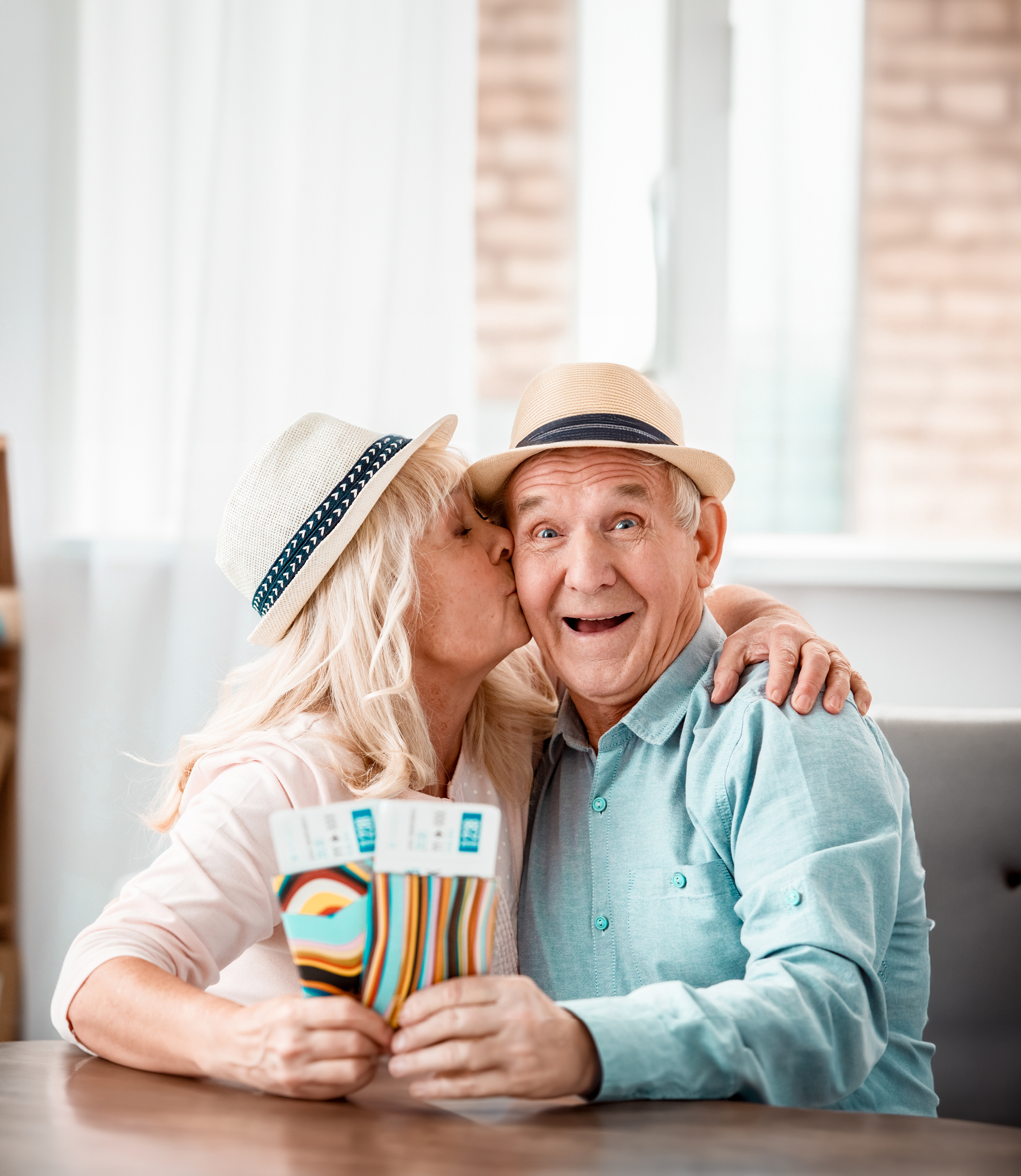 Smiling senior couple enjoying retirement, wearing sun hats and holding airline tickets for an upcoming trip.