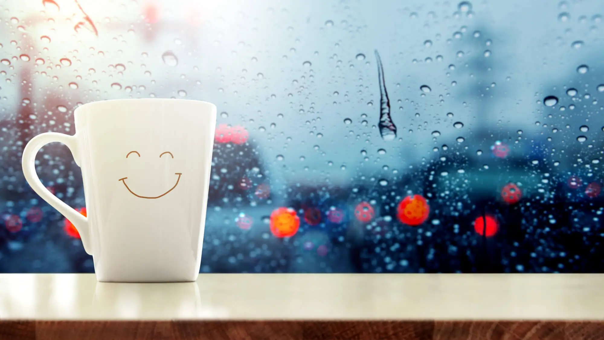 Happy Coffee Mug with smiley face on desk inside glass window, Blurred traffic jam light in city as outside view, Relaxing in cafe or Rest on rainy day