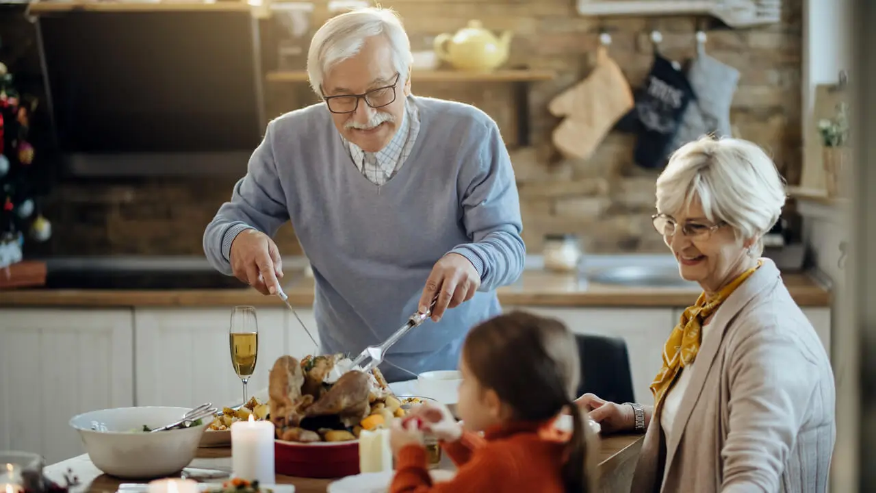 appy senior man carving turkey during Thanksgiving family lunch at home.