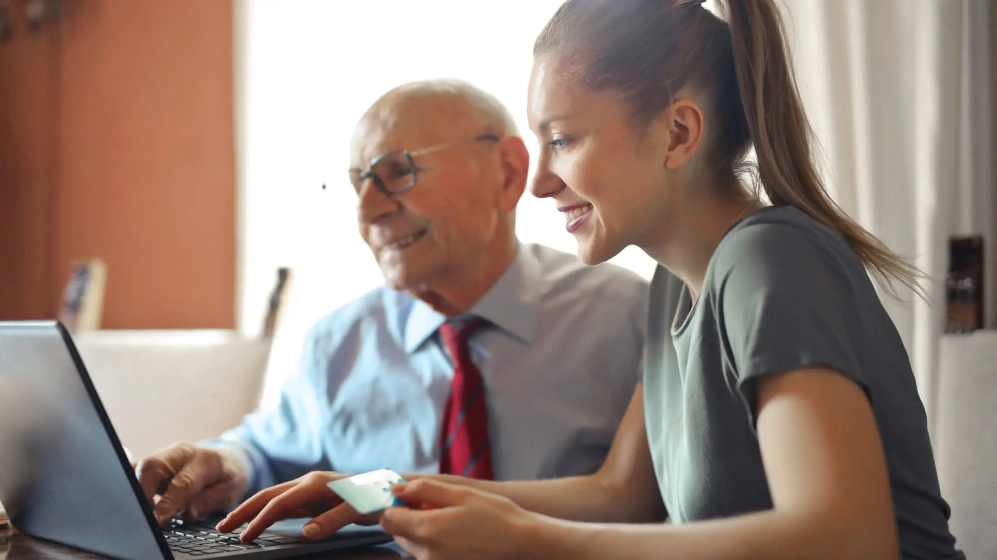 Young woman helping senior man with payment on Internet using laptop