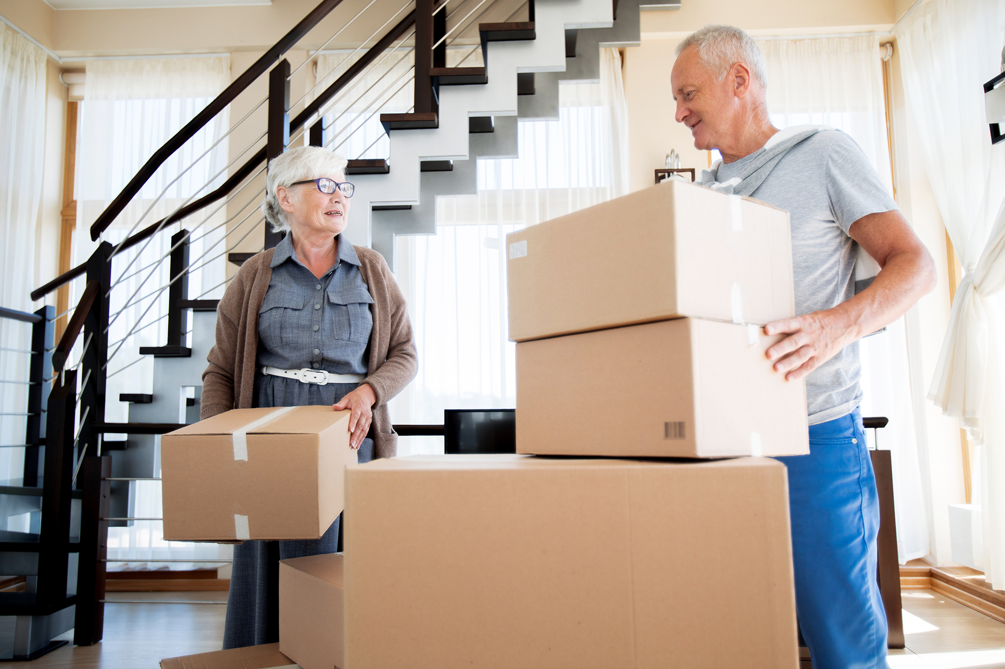A couple sorting keepsakes into boxes in a bright living room while preparing to downsize for retirement.