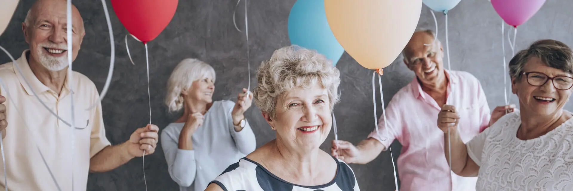 Happy senior people with colorful balloons celebrating their community's anniversary