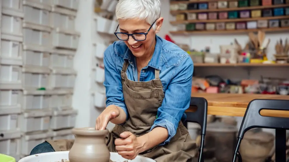 Good looking senior female potter working on pottery wheel while sitting in her workshop