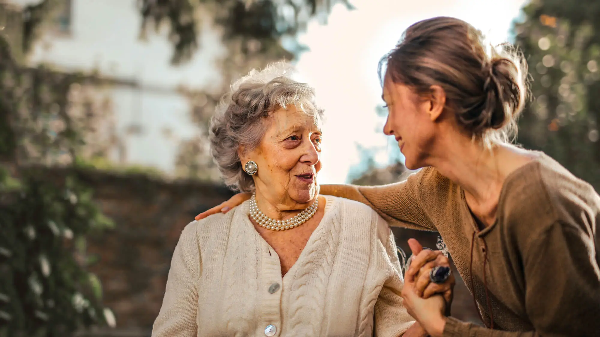 Joyful adult daughter greeting happy surprised senior mother in garden