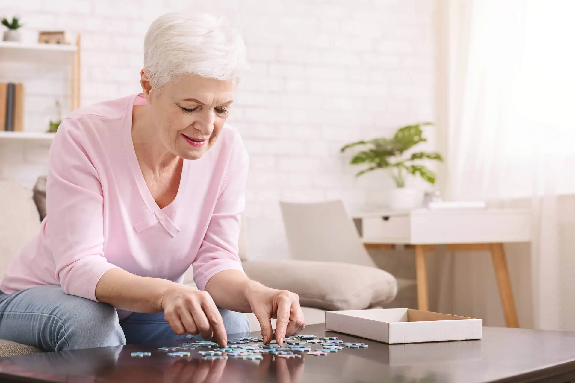 Activity can improve brain function. Elderly woman sitting at table and sorting jigsaw puzzle pieces, free space