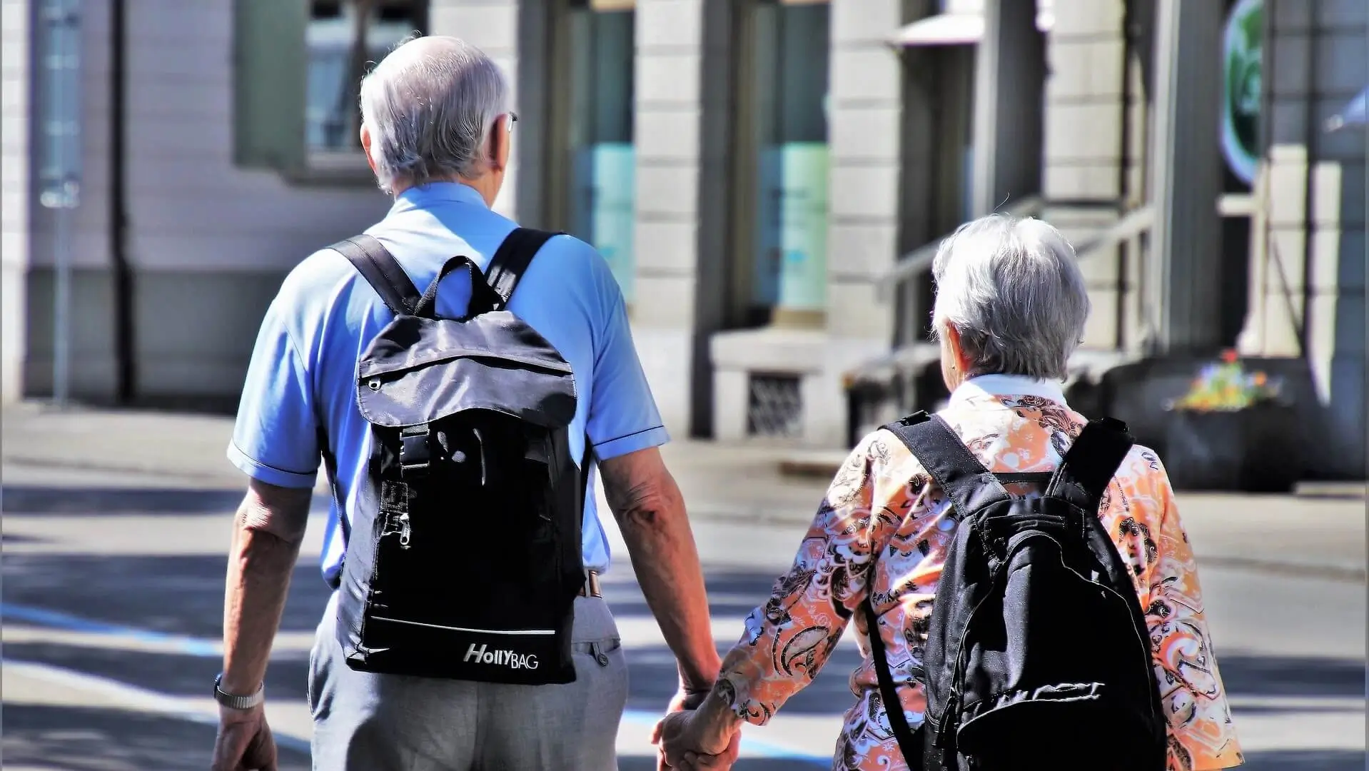 Senior couple holding hands while walking with backpacks through the city