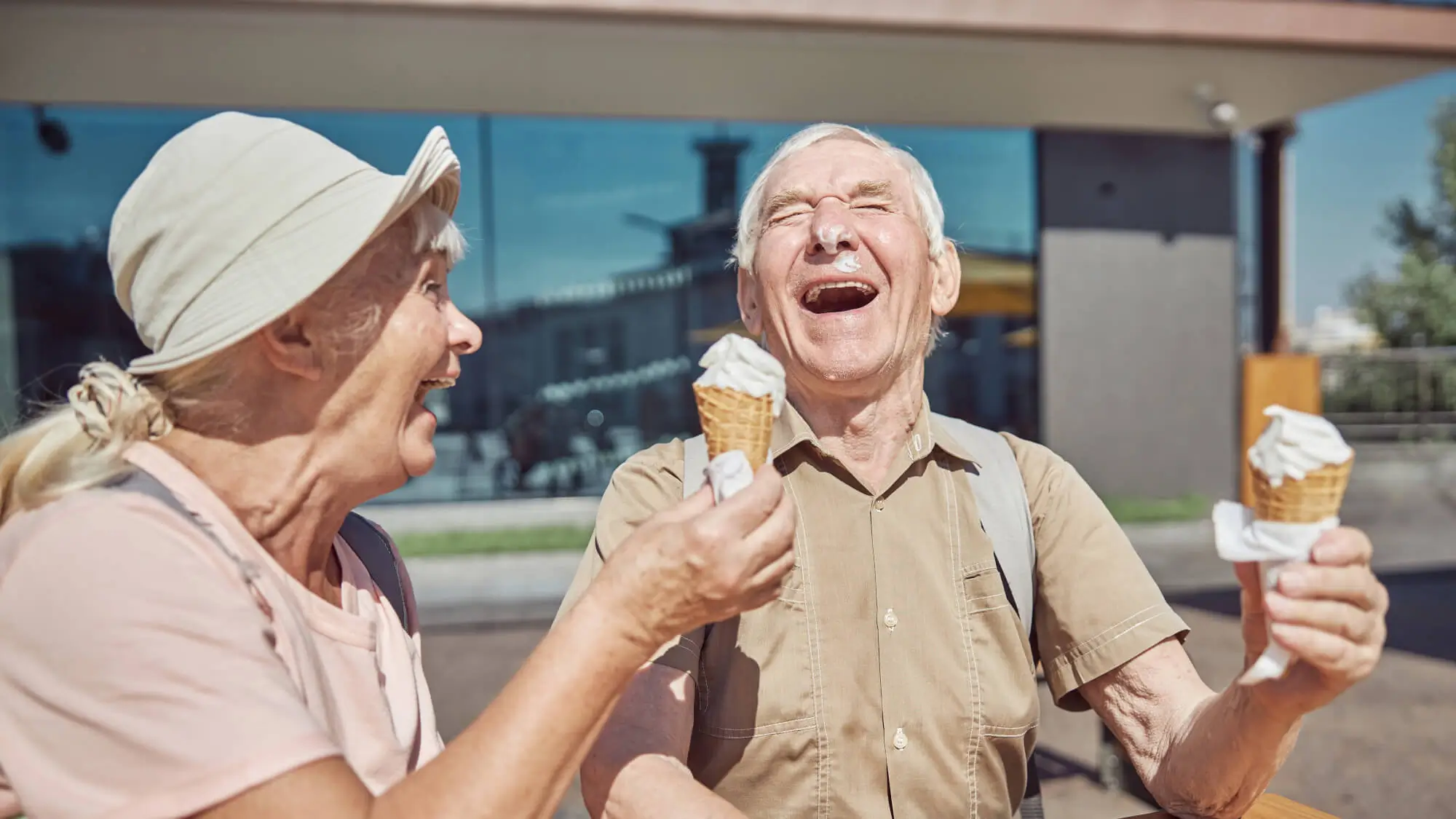 Cheerful married elderly couple with vanilla ice cream waffle cones laughing heartily at the table
