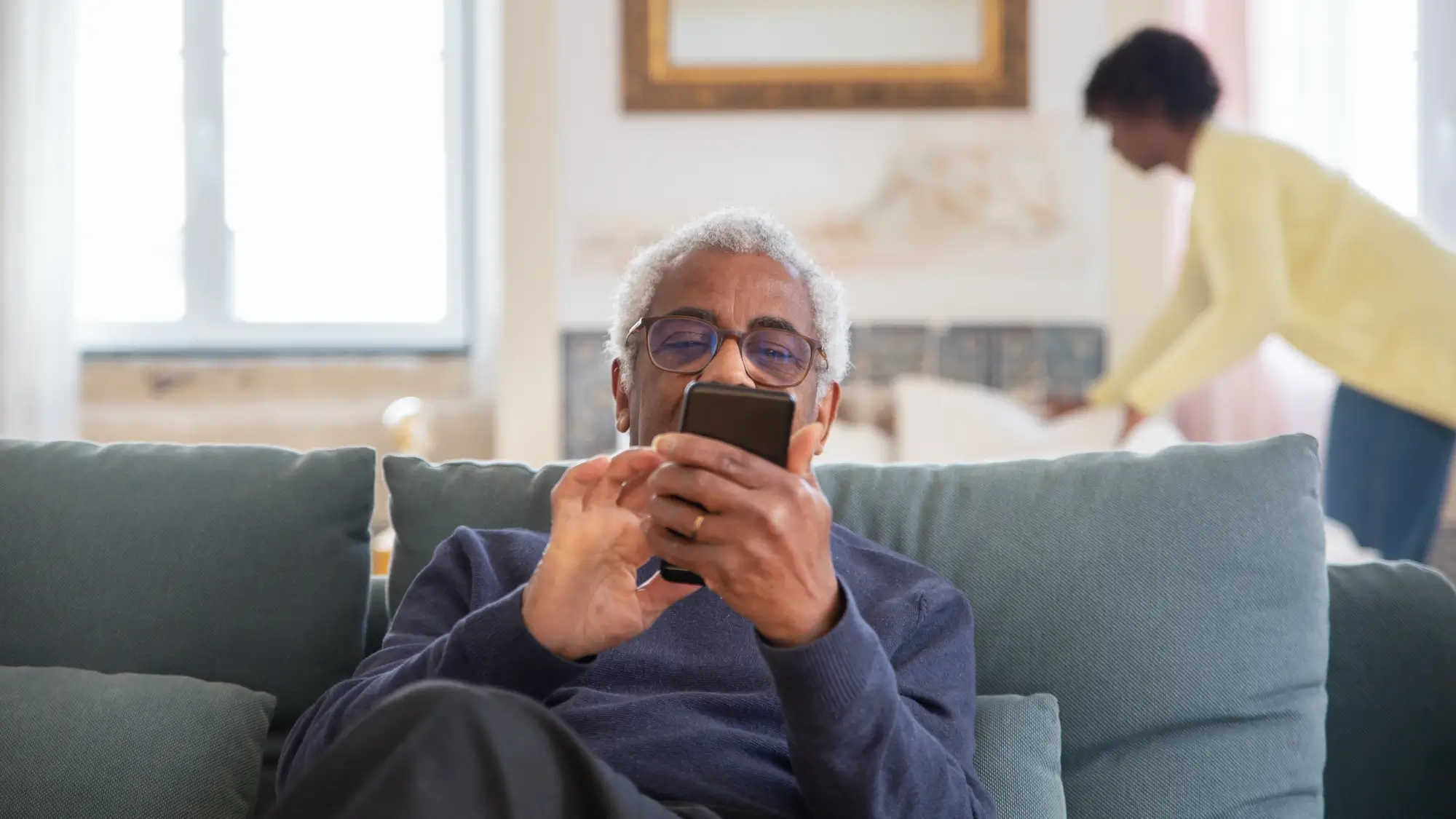 An Elderly Man Sitting on the Couch while Using His Mobile Phone