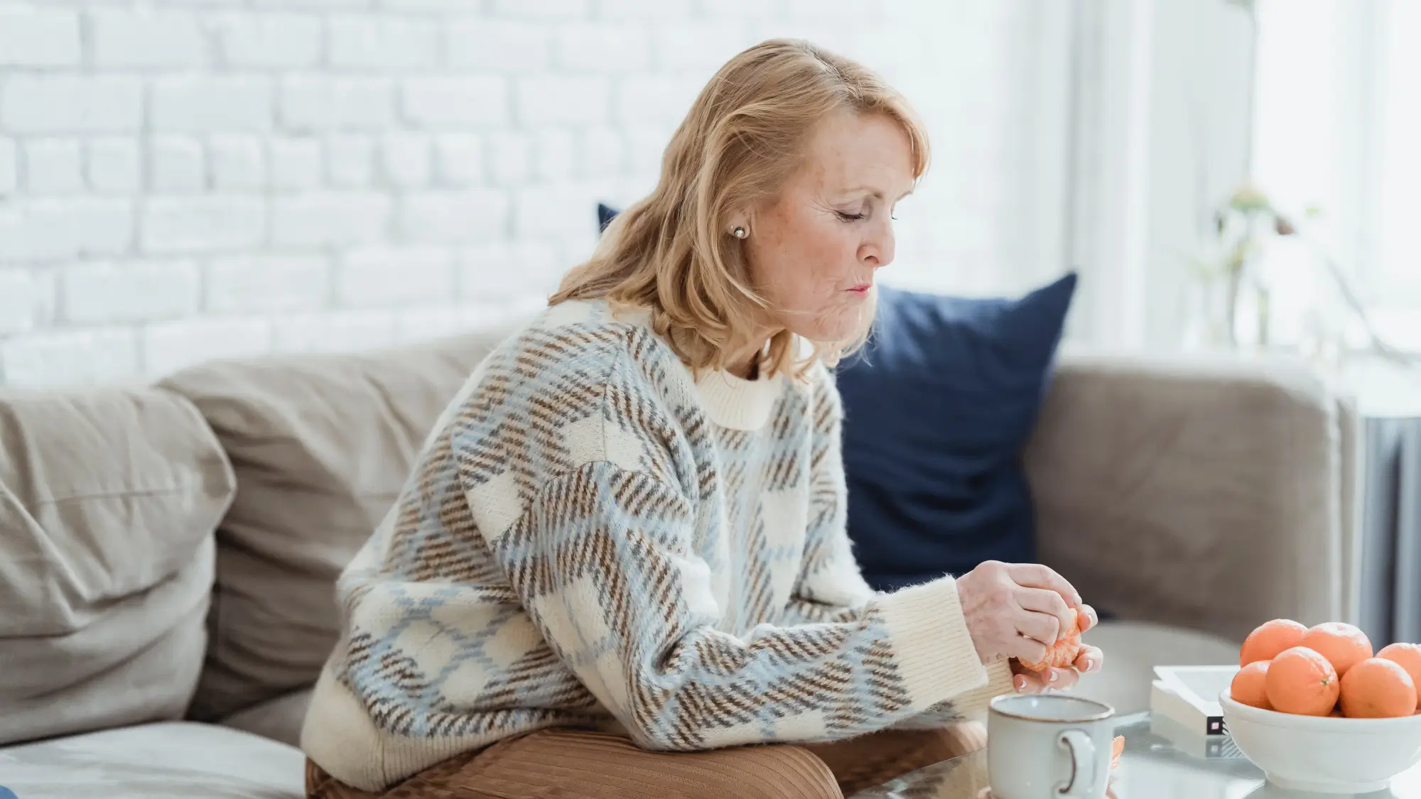 Mature woman drinking coffee and peeling mandarins while sitting on sofa