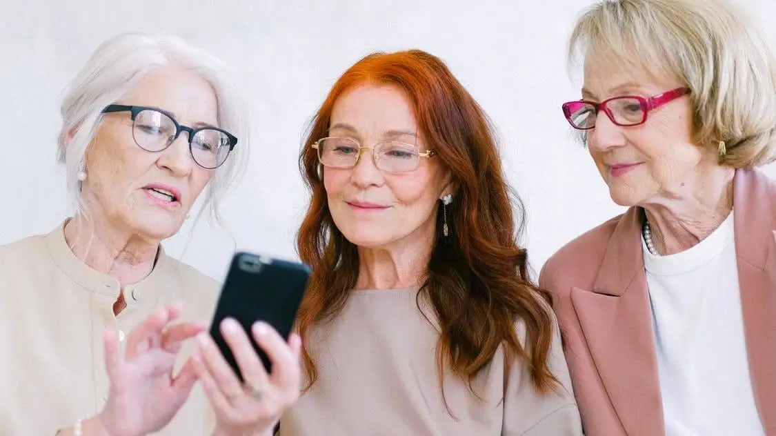 Three professionally dressed seniors viewing a mobile phone