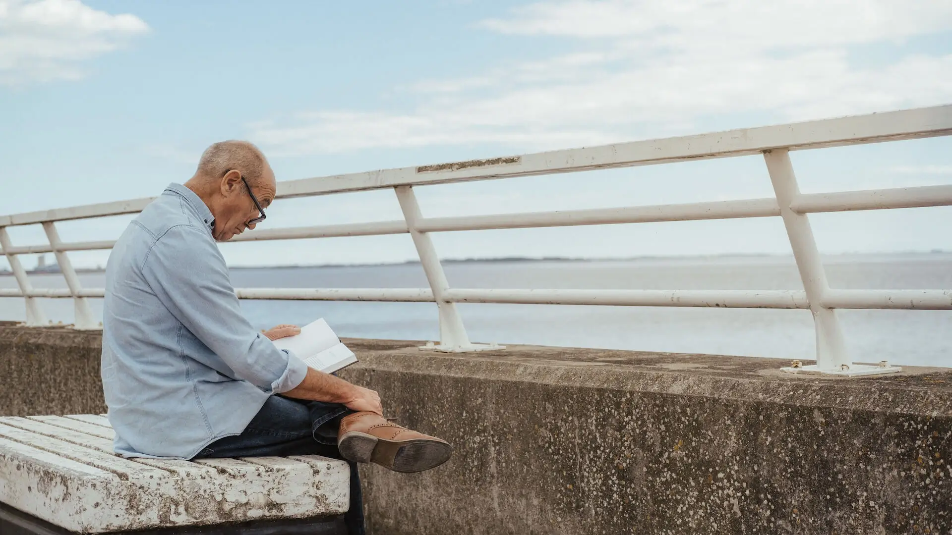 Serious senior man reading book near fence on waterfront