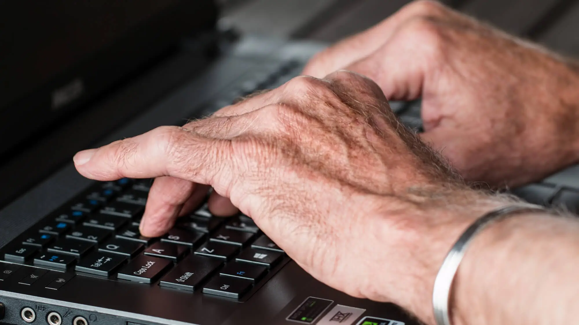 elderly hands typing on laptop