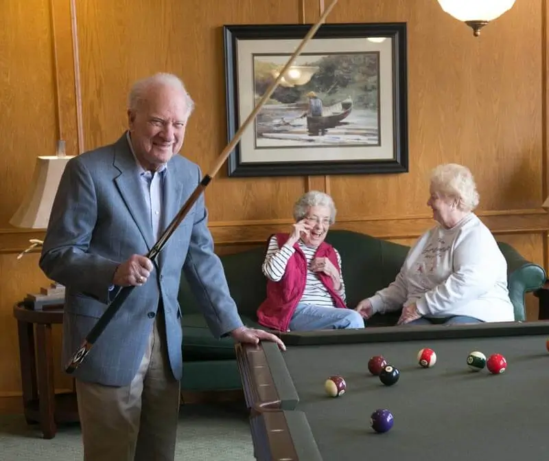 Senior friends laughing and playing billiards together.