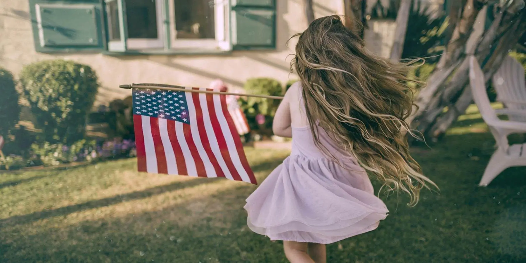Little girl running around with an American Flag at a house.
