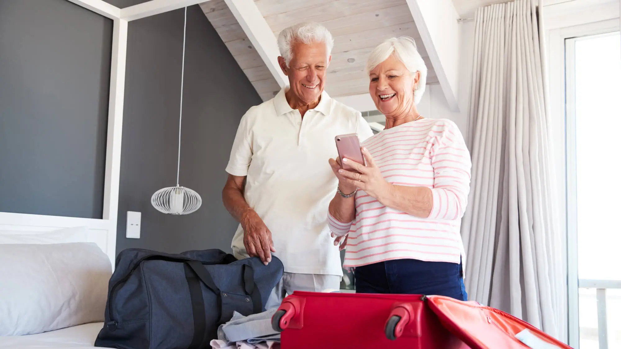 Senior Couple Look At Mobile As They Check In To Vacation Rental