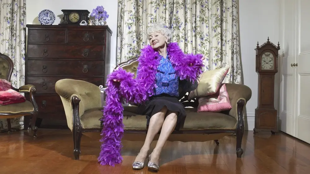 Happy senior woman wearing feather boa sitting on sofa in living room