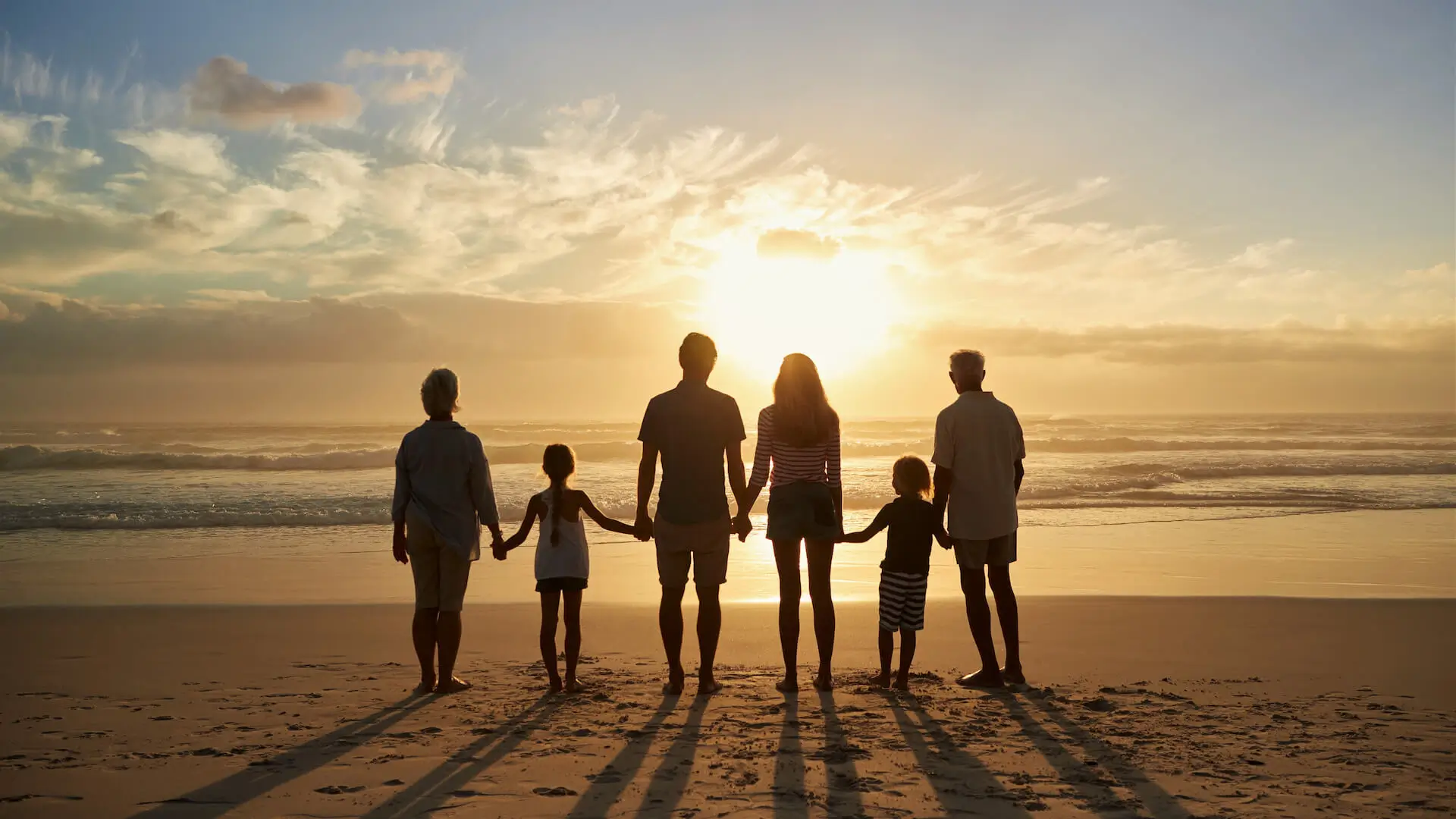 Rear View Of Multi Generation Family Silhouetted On Beach